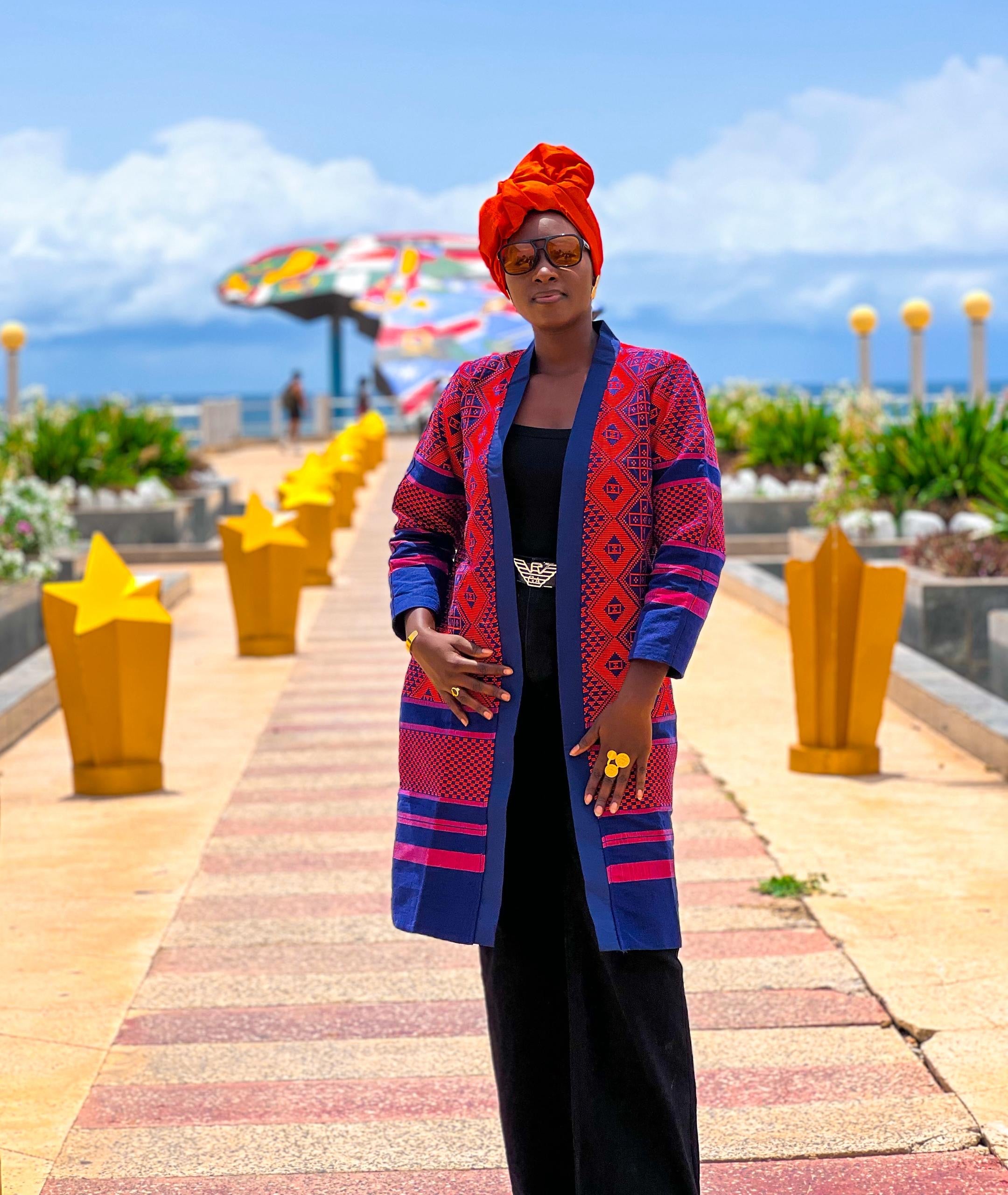 Model wearing Kanoo Hand Woven Jacket, showcasing its vibrant colors and traditional patterns against a scenic background.