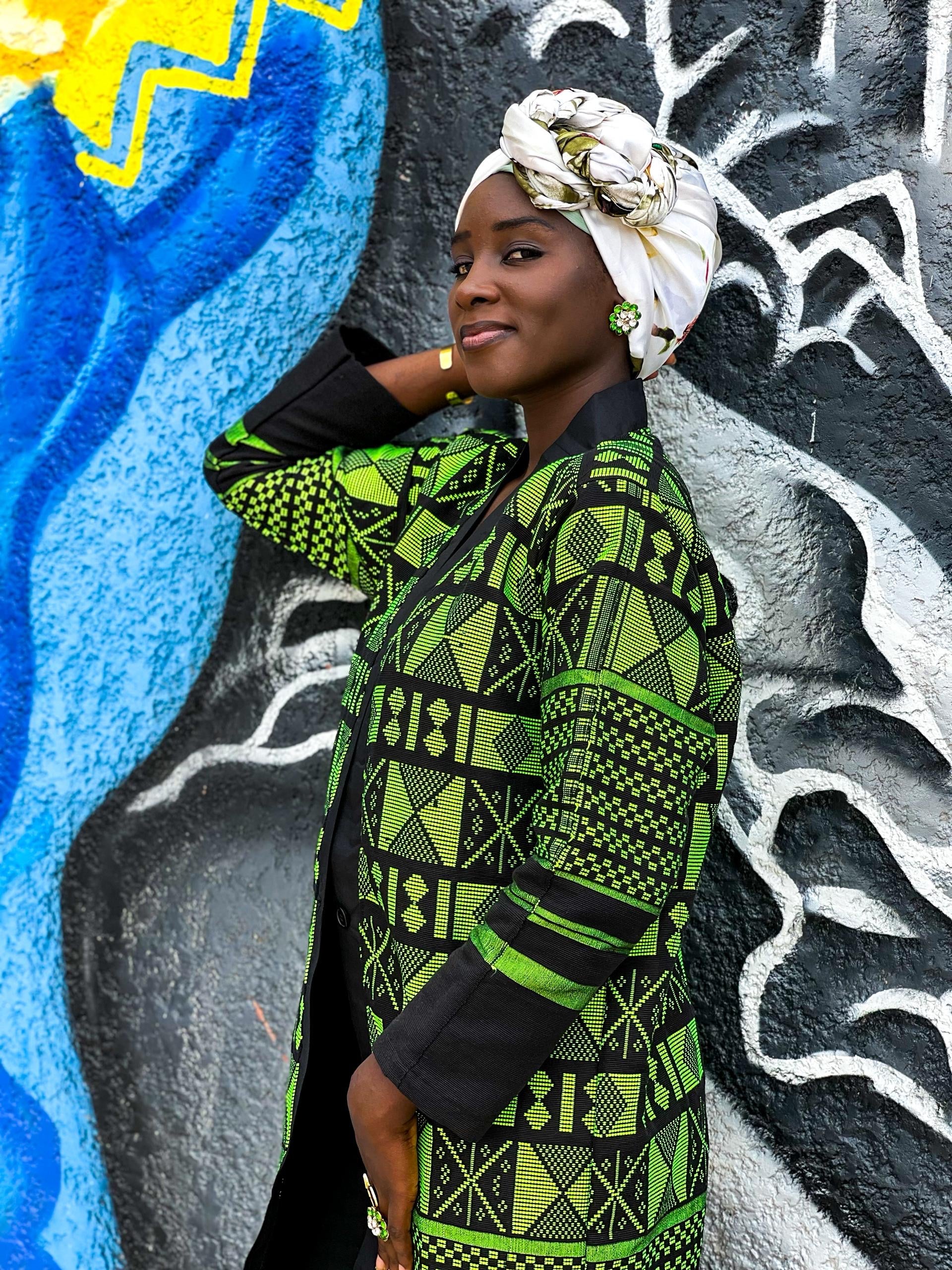 Kanoo Hand Woven Jacket showcased by a woman against a vibrant mural, highlighting African craftsmanship and heritage.
