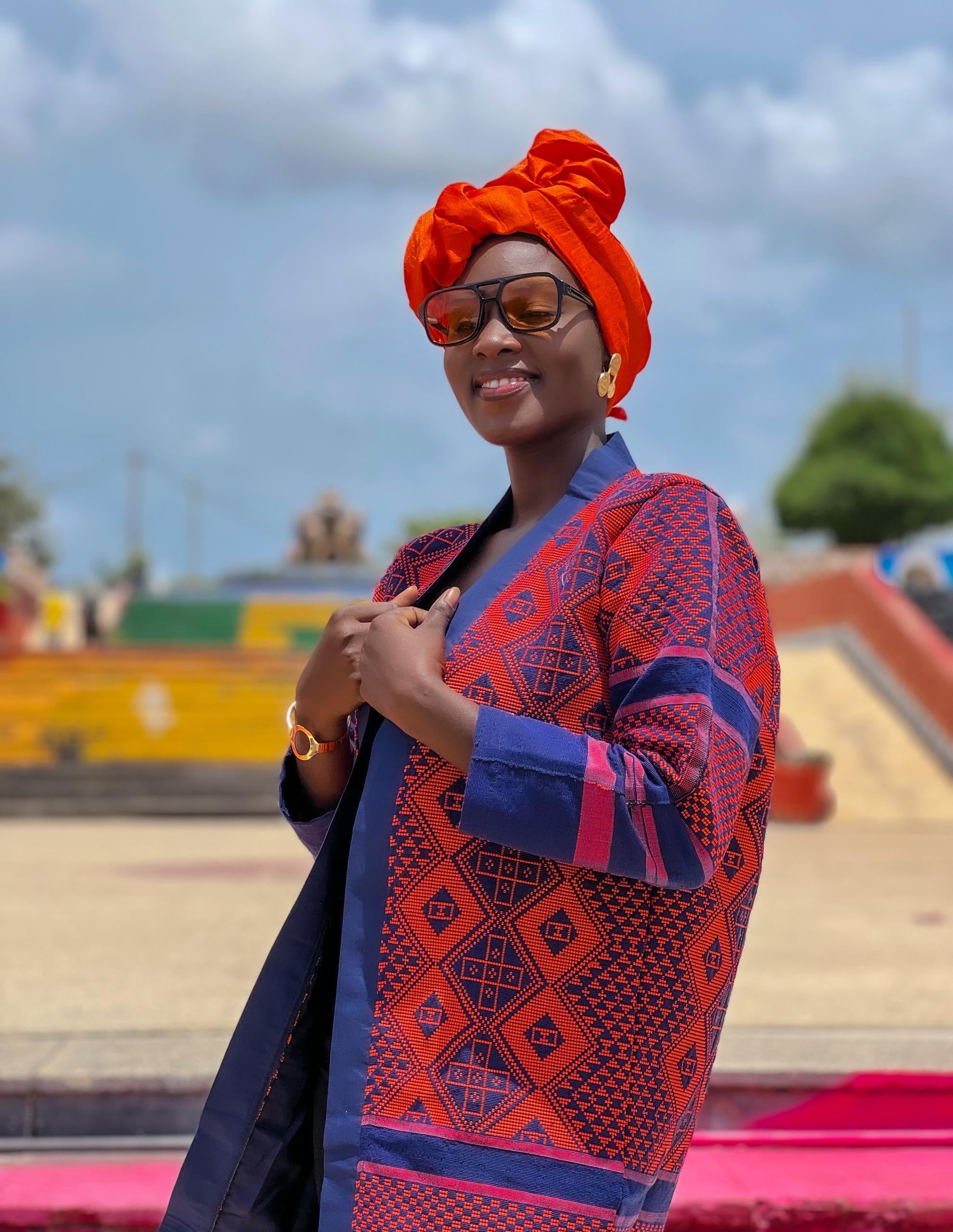 A woman wearing the Kanoo Hand Woven Jacket, showcasing vibrant patterns and colors, representing Senegalese heritage.